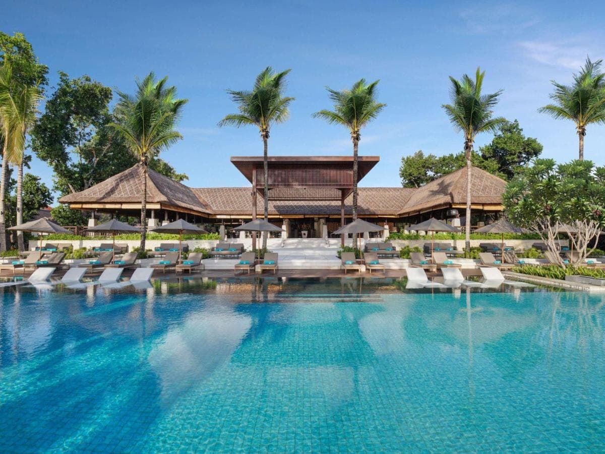a pool at a resort with chairs and palm trees at Novotel Bali Benoa in Nusa Dua