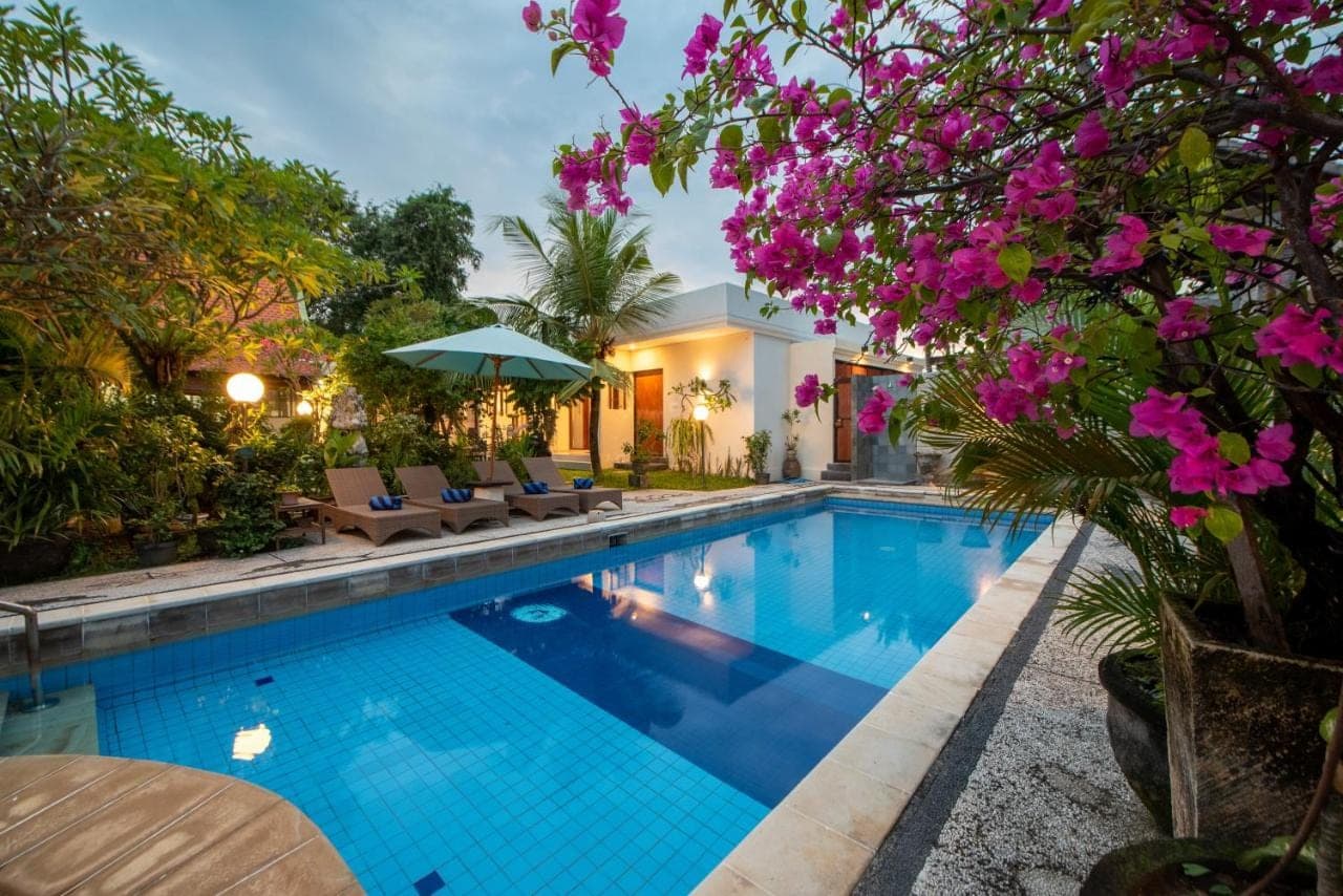 a swimming pool with chairs and pink flowers at Baruna Homestay Sanur in Sanur