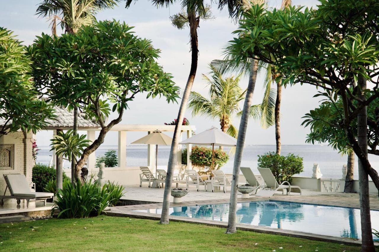 a pool with palm trees and chairs and the ocean at Dhauteya Villa in Amed