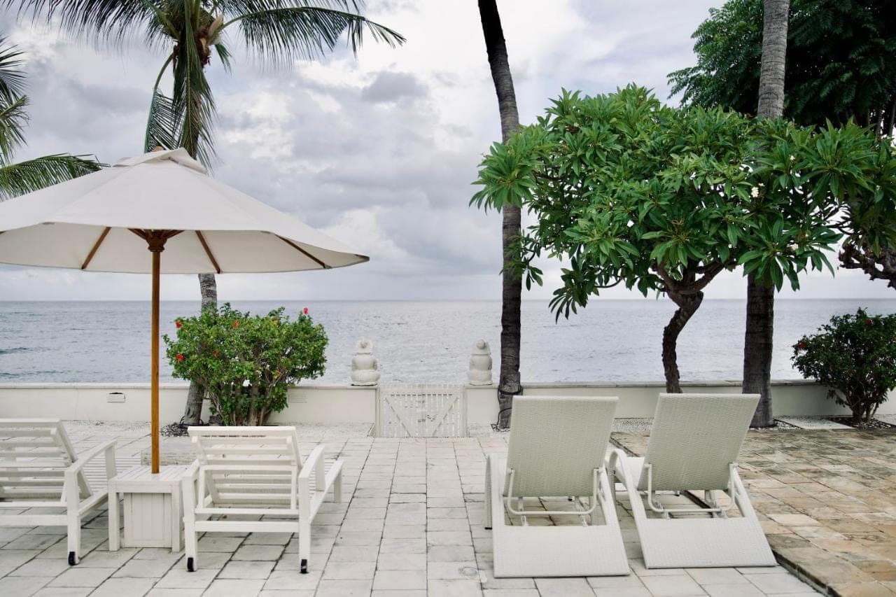a patio with chairs and an umbrella and the ocean at Dhauteya Villa in Amed