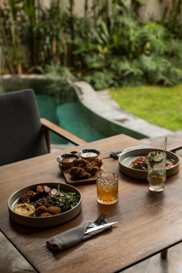 a wooden table with plates of food and drinks on it at Surf Motel Bali in Canggu