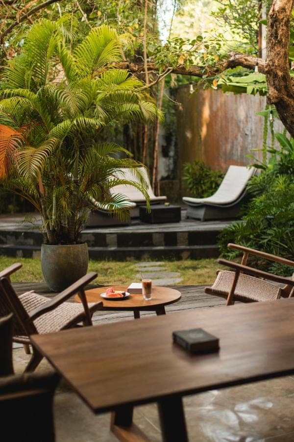 a patio with a table and chairs and palm trees at Surf Motel Bali in Canggu