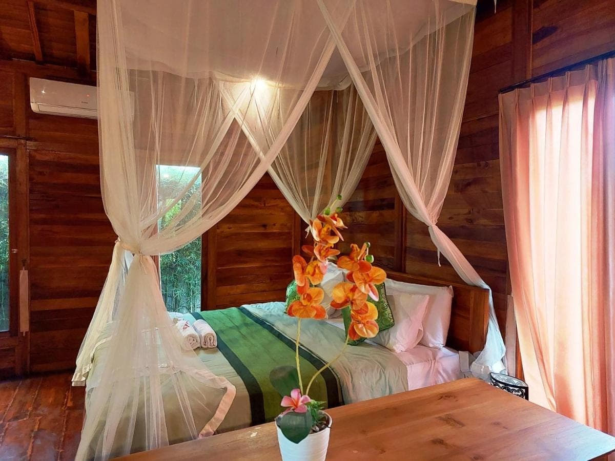 a bedroom with a bed with curtains and a table at Shivananda Antique Villas by EPS in Ubud