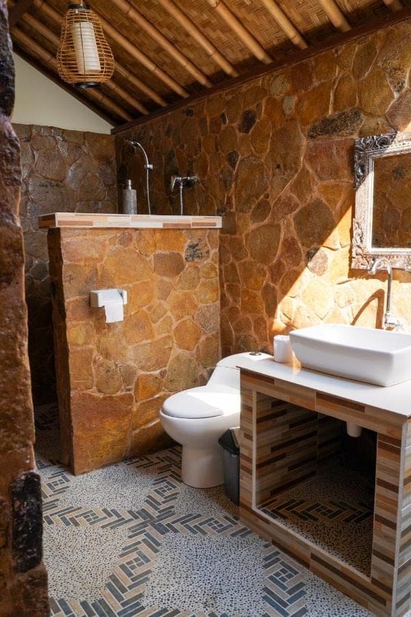 a stone bathroom with a toilet and a sink at Bamboo Bali Hill Bungalows in Amed