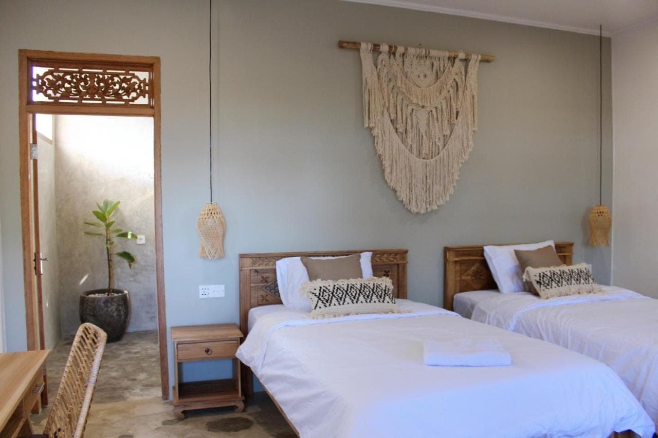 a bedroom with two beds and a table and a window at The Inn Possible in Uluwatu