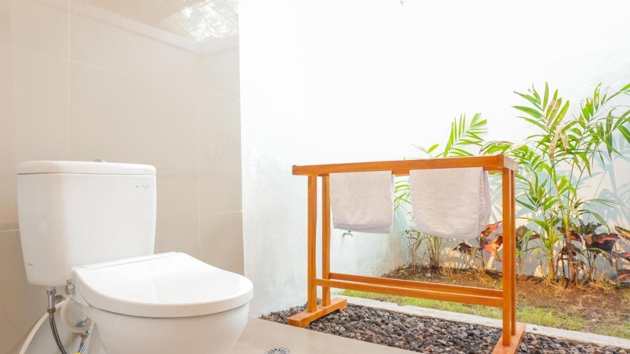 a bathroom with a toilet and a window with plants at Sunburn Villa in Nusa Dua