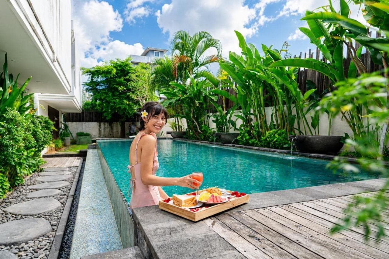 a woman holding a box of food next to a pool at D'Green Nirava Kuta By Reccoma in Kuta