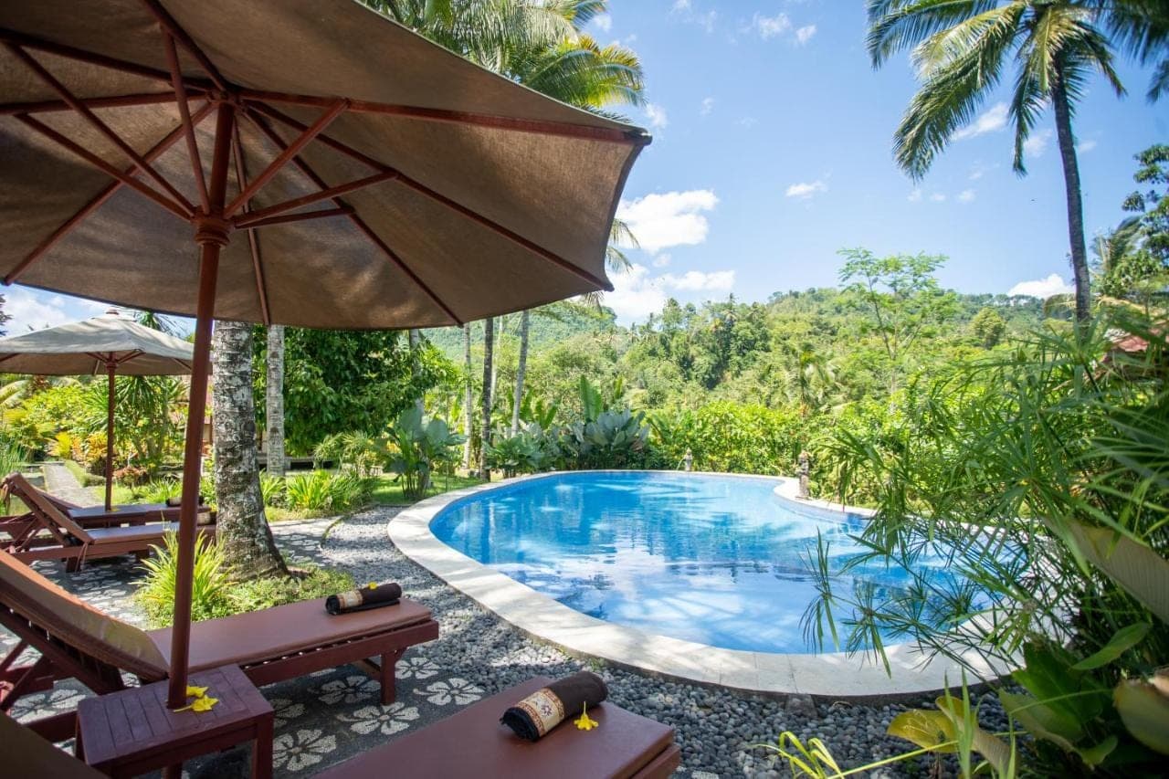a pool at a resort with an umbrella and chairs at Villa Uma Ayu Sidemen in Sidemen