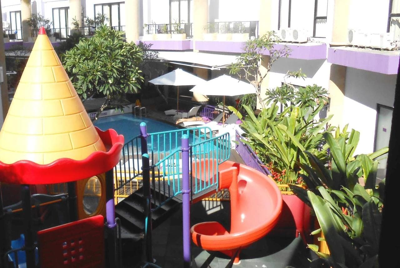 a balcony with a playground and a pool in a building at Kuta Central Park Hotel in Kuta