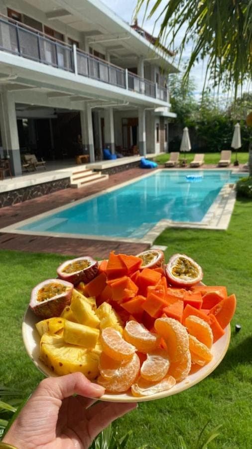 a person holding a plate of fruit next to a pool at Nala's Home in Uluwatu