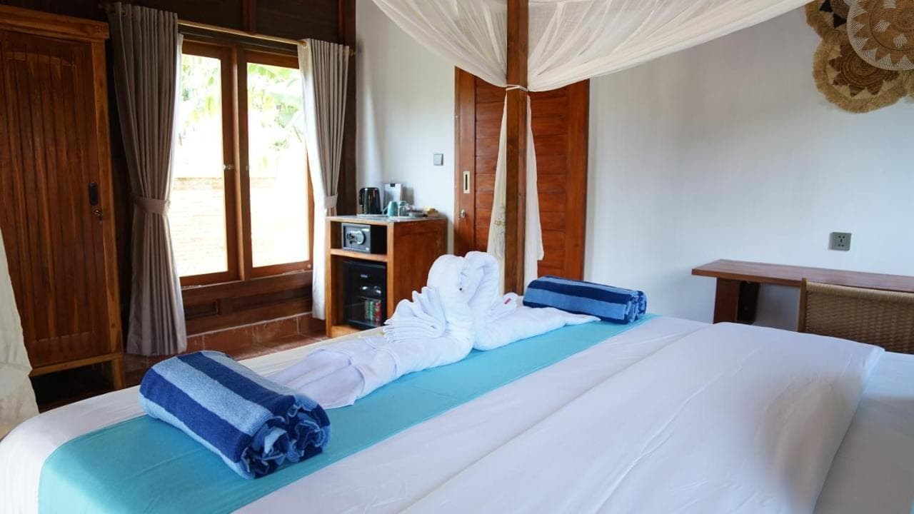 a bedroom with a large white bed with blue pillows at Kubu Kangin Resort in Amed