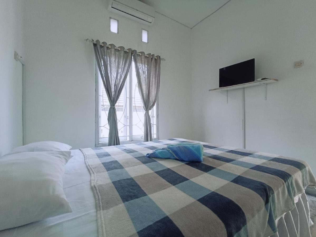 a bedroom with a bed with a checked blanket and a window at Pigeon House Nusa Dua in Nusa Dua