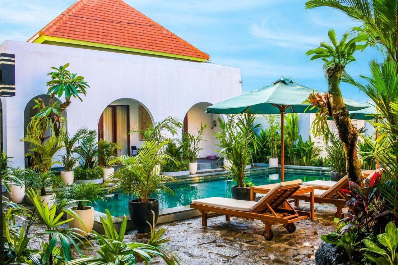 a resort pool with chairs and an umbrella at Umi Umi Homestay Sanur in Sanur