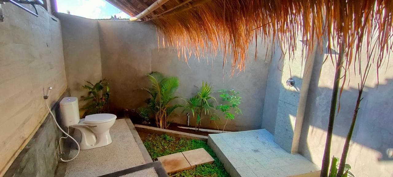 a bathroom with a toilet and some plants at Yogi Beach Cabin in Amed