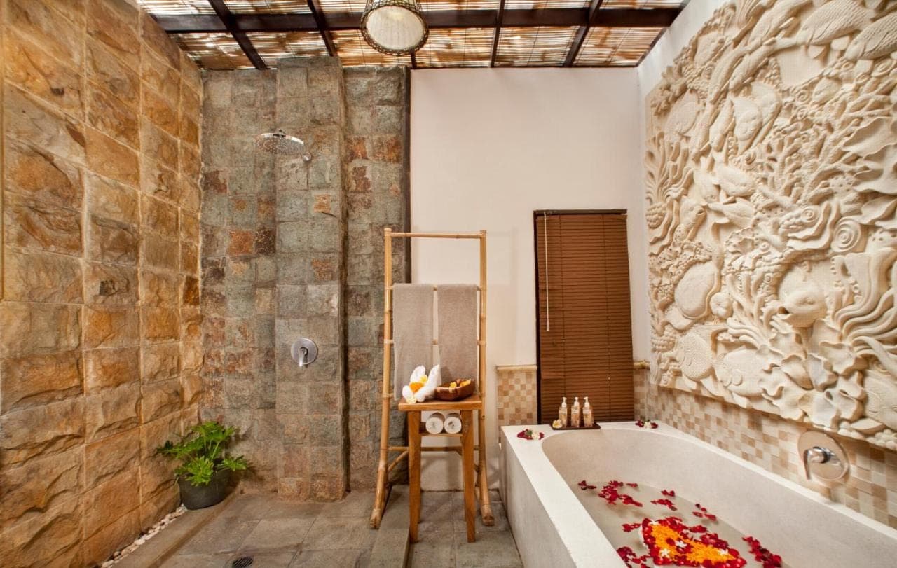 a bathroom with a tub and a stone wall at Arimba at Bisma in Ubud