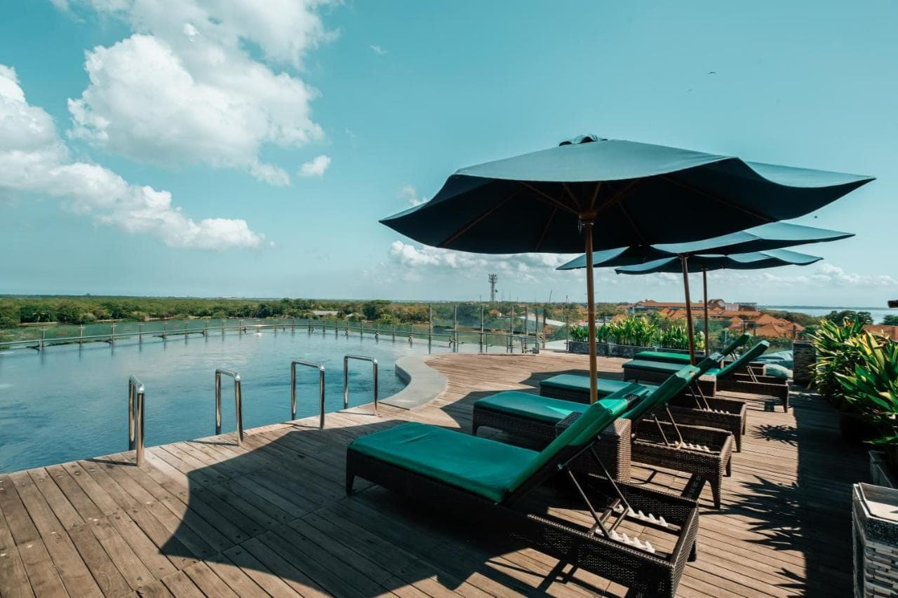 a group of chairs and umbrellas next to a pool at The Nest Hotel Nusa Dua in Nusa Dua