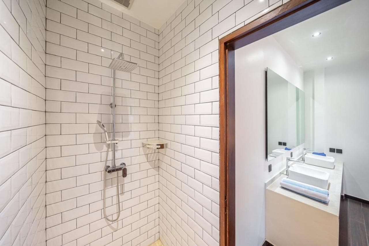 a white tiled bathroom with a shower and a sink at The Cokelat Amed in Amed