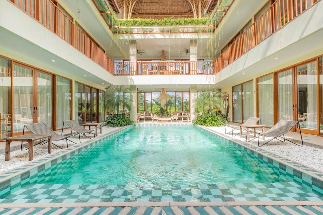 a swimming pool with chairs and tables in a building at Ellisani Bali in Canggu