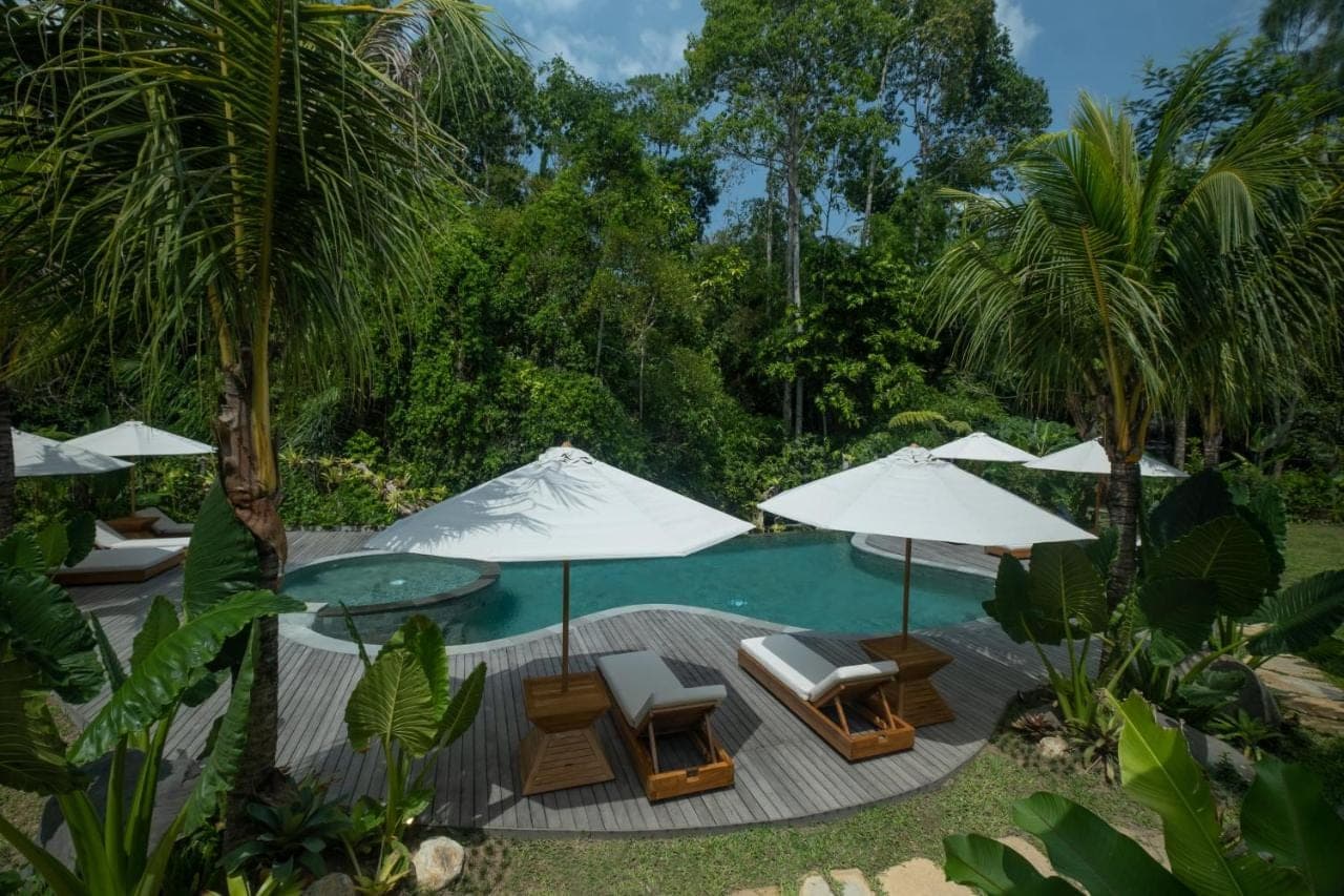a swimming pool with chairs and umbrellas and a pool at Samujha Ubud Resort in Ubud