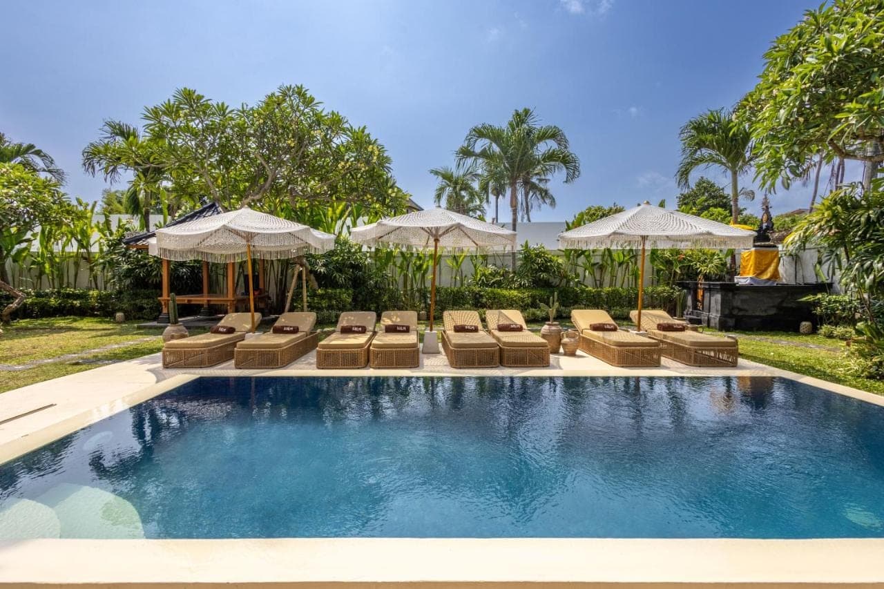 a swimming pool with lounge chairs and umbrellas at KALM Bali in Canggu