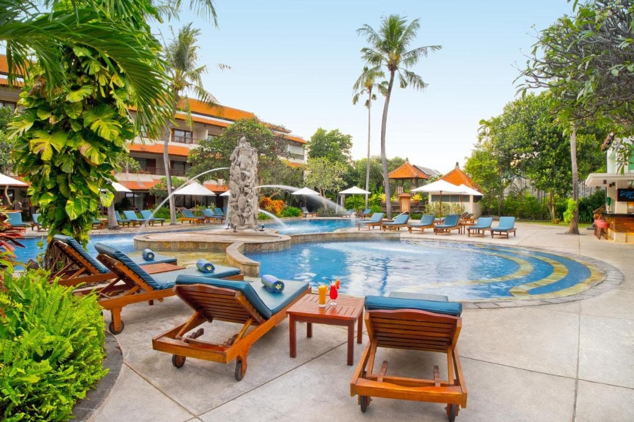 a pool at a resort with chairs and a fountain at Bali Rani Hotel in Kuta