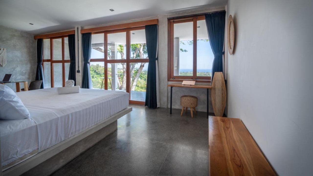 a bedroom with a bed and a desk and windows at Padawatu Villas in Uluwatu