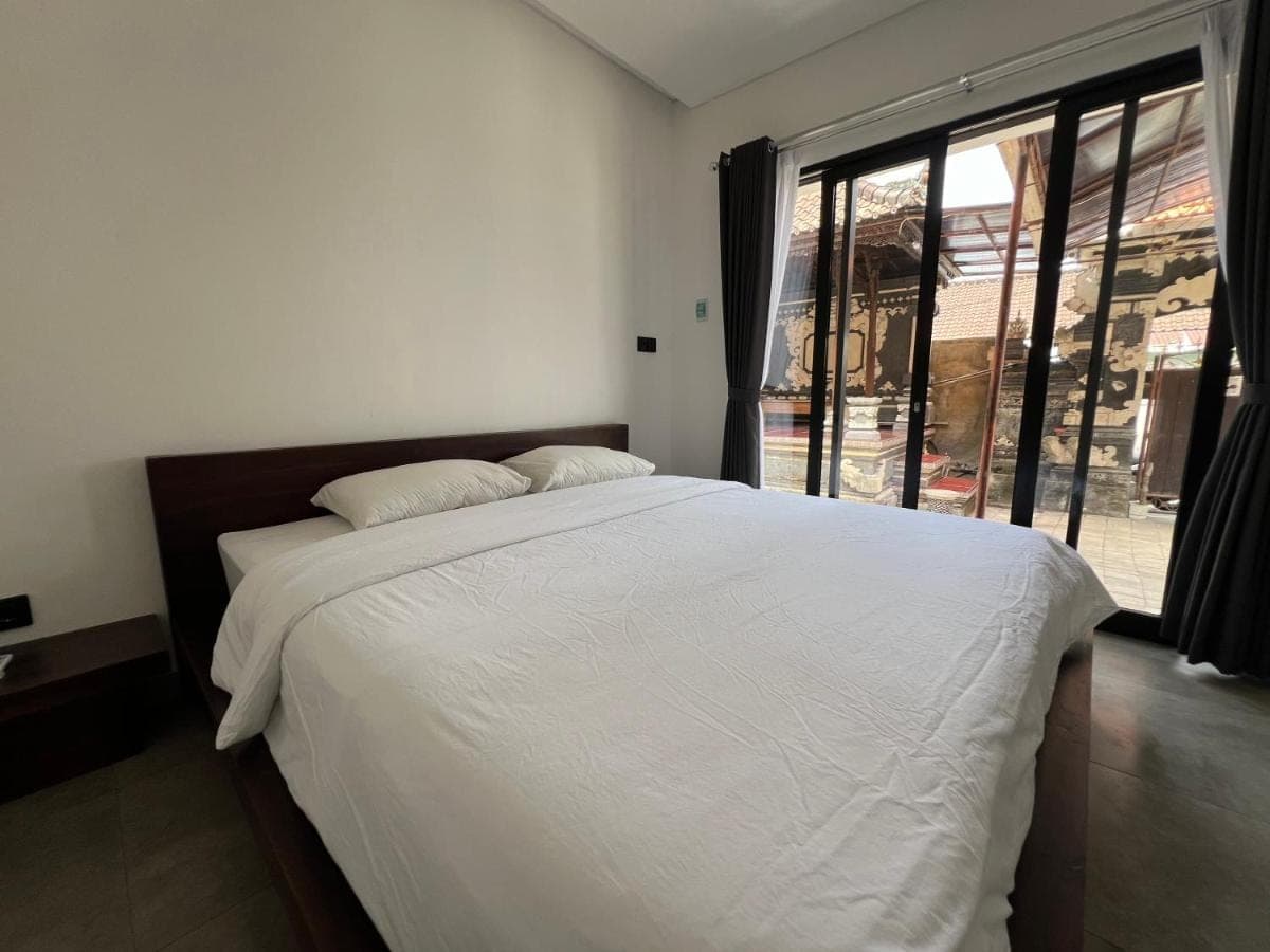 a bedroom with a large white bed with a large window at Uger House Seminyak in Seminyak