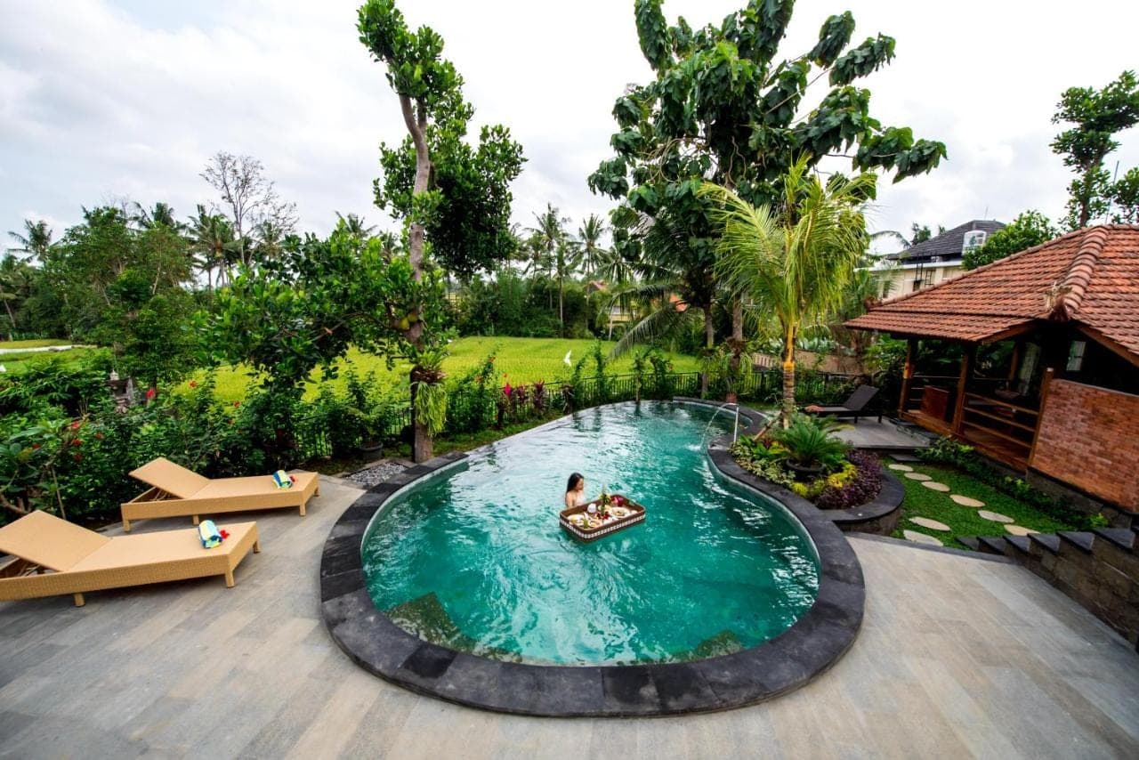 a pool at a resort with two people in a boat in it at Puri Kobot Ubud in Ubud