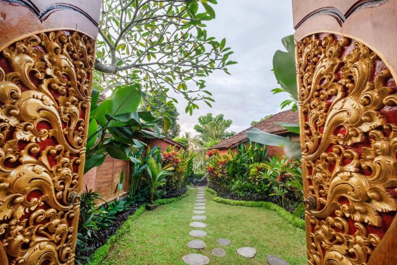 a path through a garden with houses in the background at Puri Kobot Ubud in Ubud
