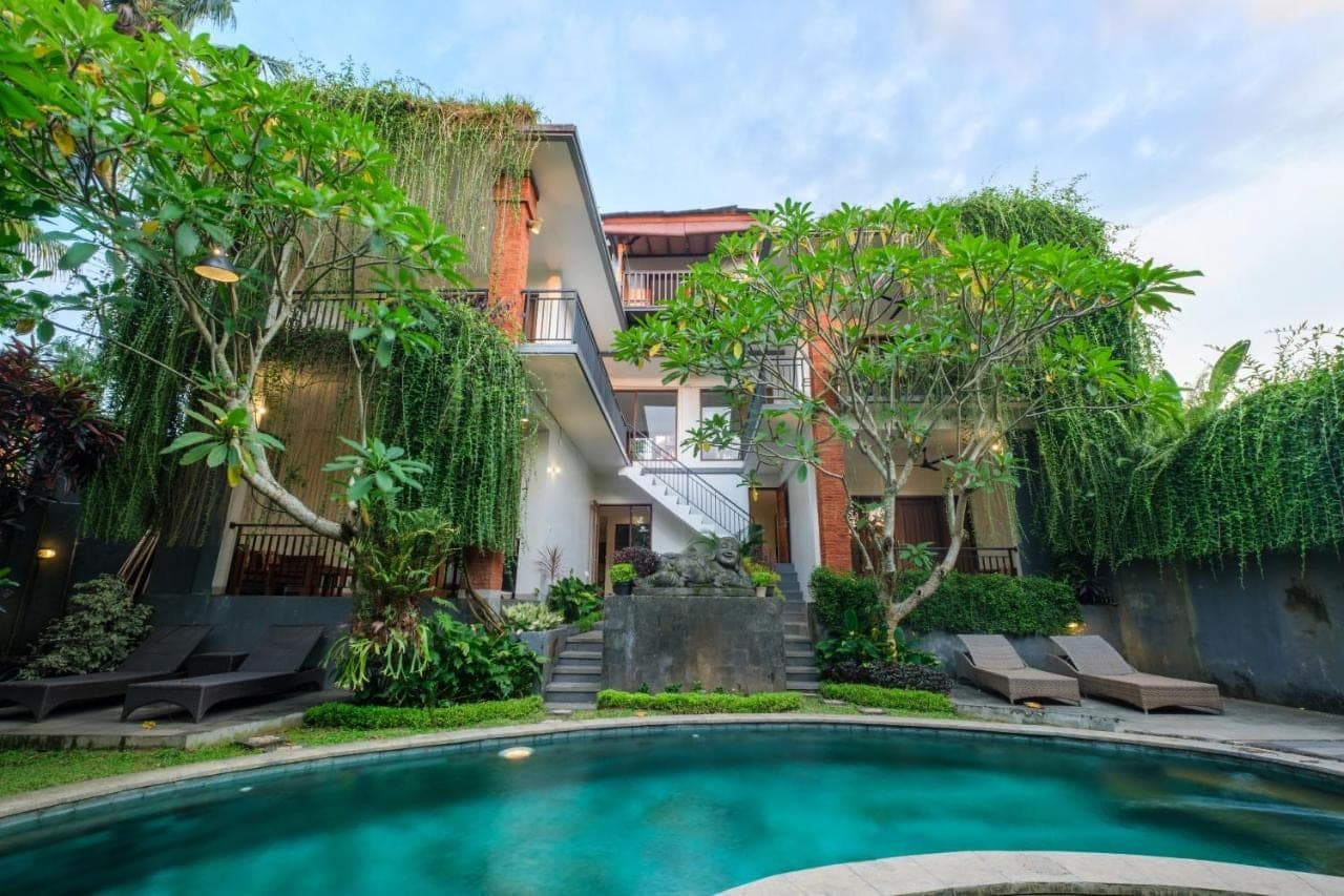 a swimming pool in front of a building with trees at Puri Kobot Ubud in Ubud