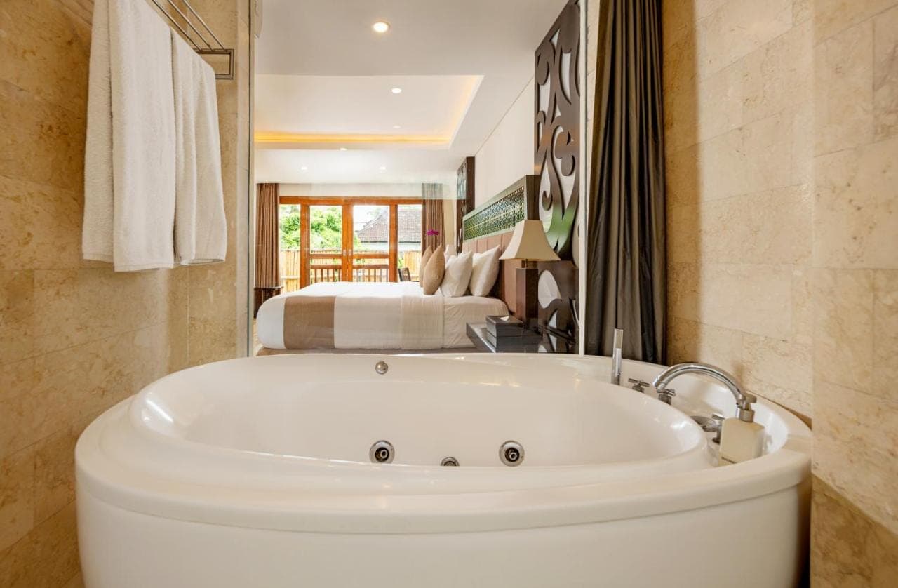 a bath tub in a bathroom with a bedroom at Villa Kayu Raja in Seminyak