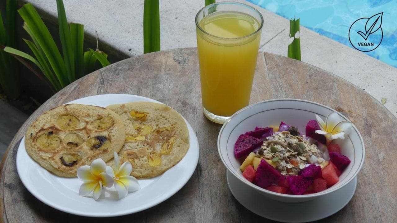 a table with a plate of food and a bowl of fruit and a drink at Mojosurf Camp Canggu in Canggu