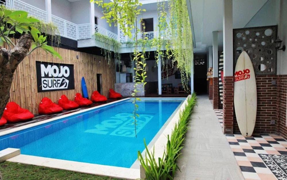 a pool with red chairs and a surfboard next to a building at Mojosurf Camp Canggu in Canggu