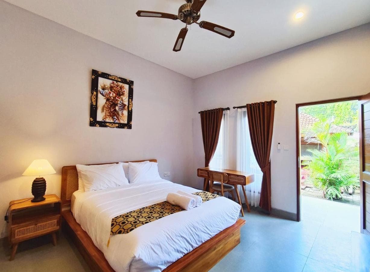 a bedroom with a bed and a desk and a window at Vinandaka Homestay in Sanur
