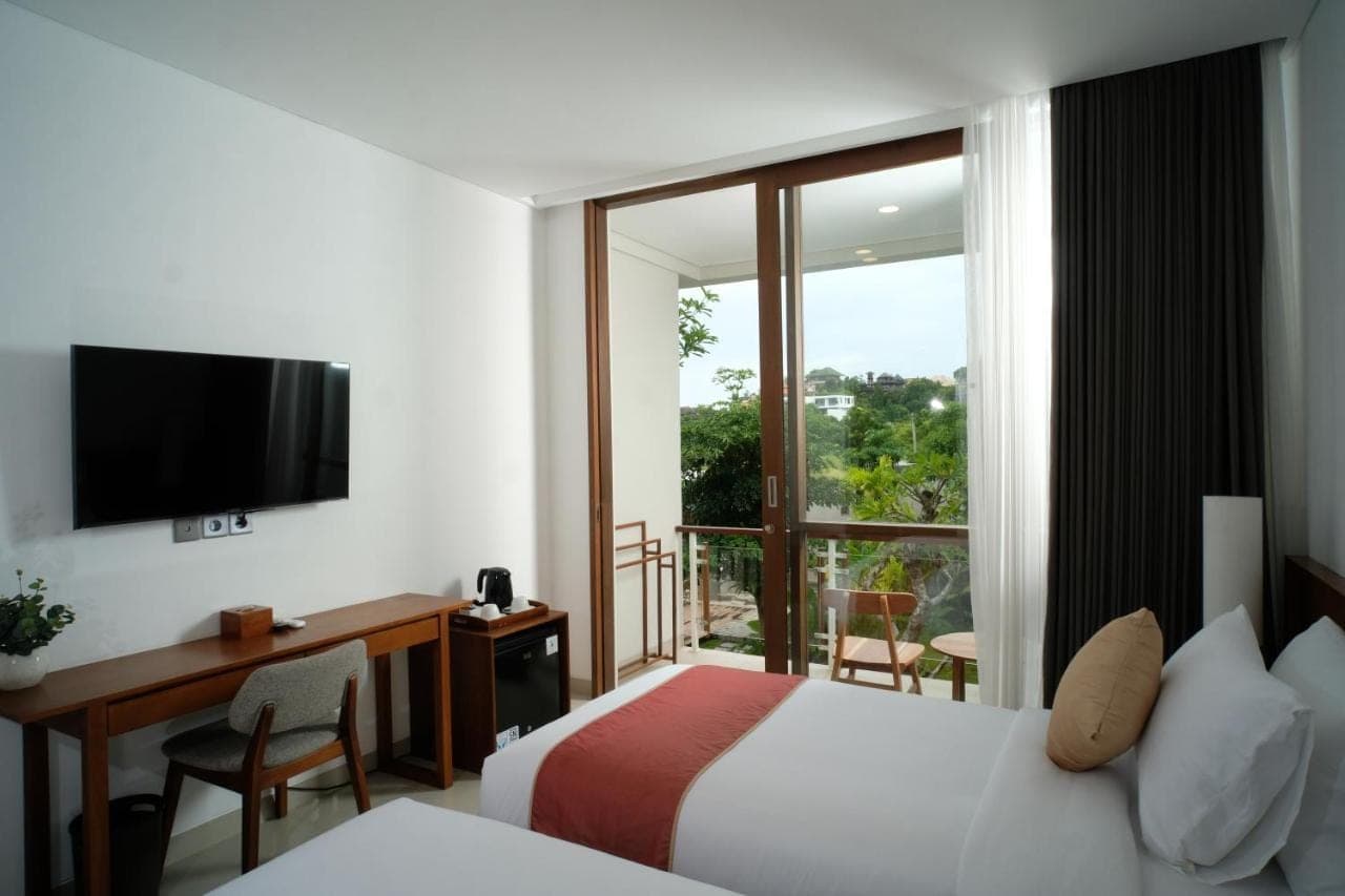 a hotel room with a bed and a desk and a window at The Ledge Uluwatu in Uluwatu
