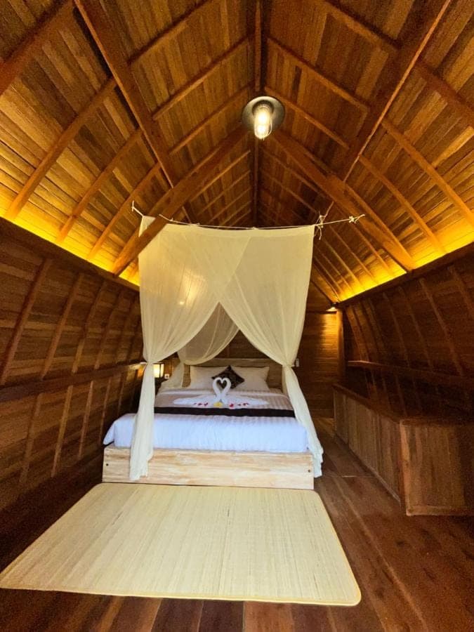a bed in a wooden room with a mosquito net at Lumbung Kembar Sidemen in Sidemen