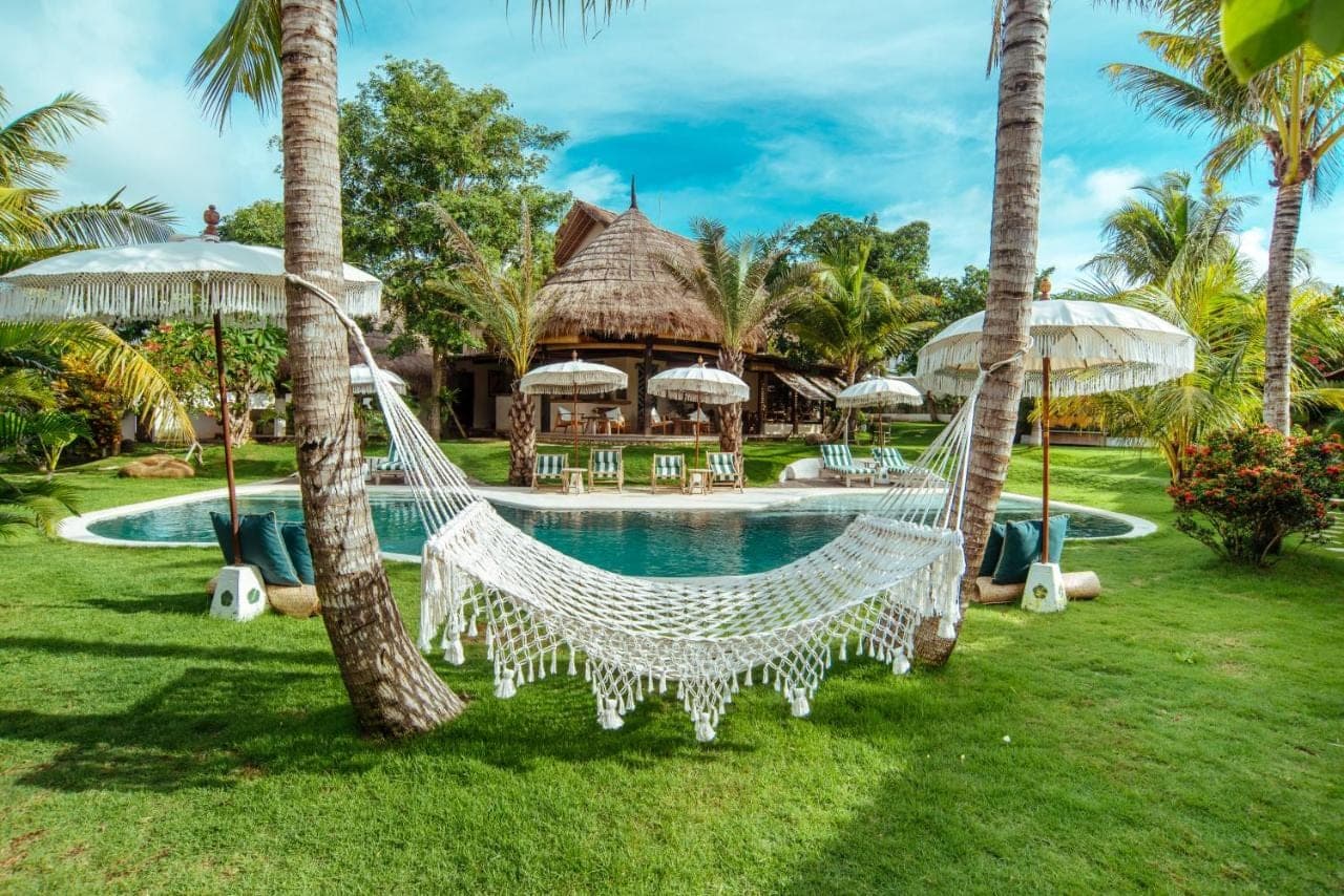 a hammock in front of a resort with a pool at Mule Malu in Uluwatu
