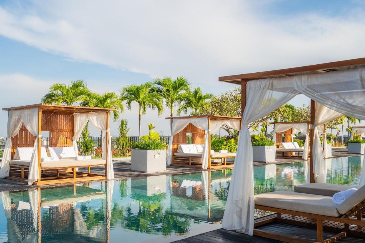 a resort with a pool with beds and trees at Cross Paasha Bali Seminyak in Seminyak