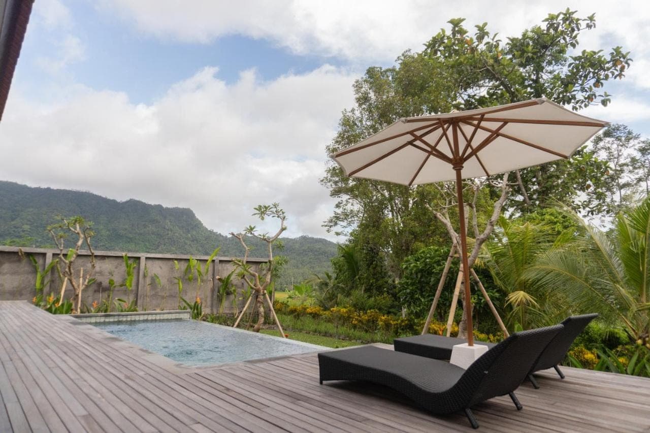 a deck with a chair and an umbrella and a pool at The Ume Sidemen Villas in Sidemen