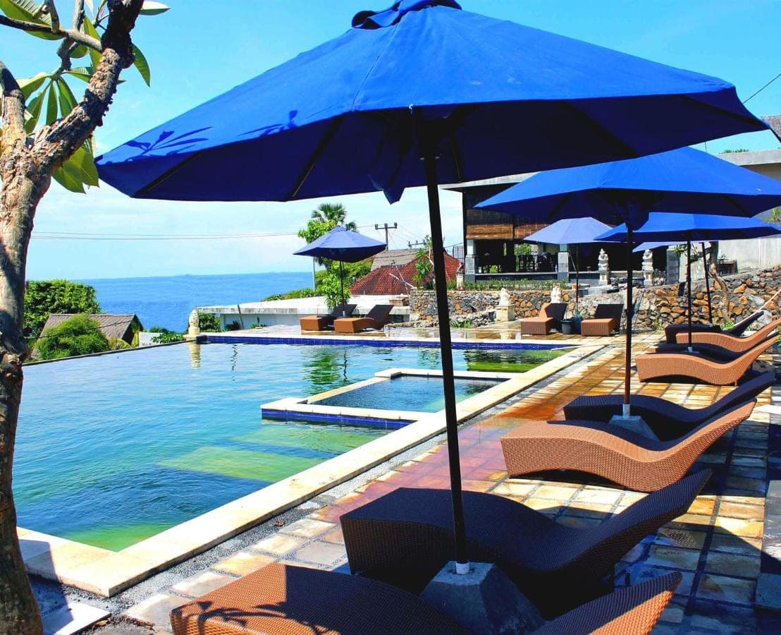 a pool with chairs and umbrellas next to a swimming pool at Bali Bhuana Villas in Amed