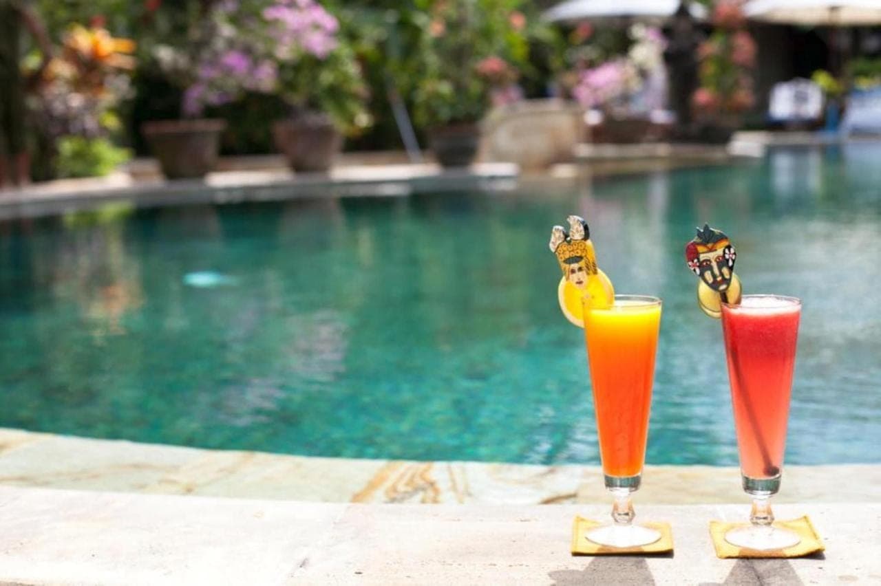two drinks sitting on a table next to a swimming pool at Tamukami Hotel in Sanur