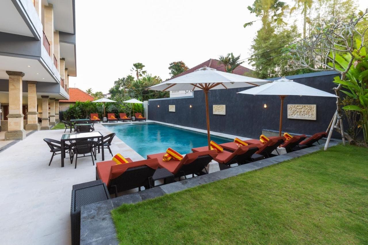 a pool with chairs and tables and umbrellas next to at Kubu Petitenget Suite Seminyak in Seminyak