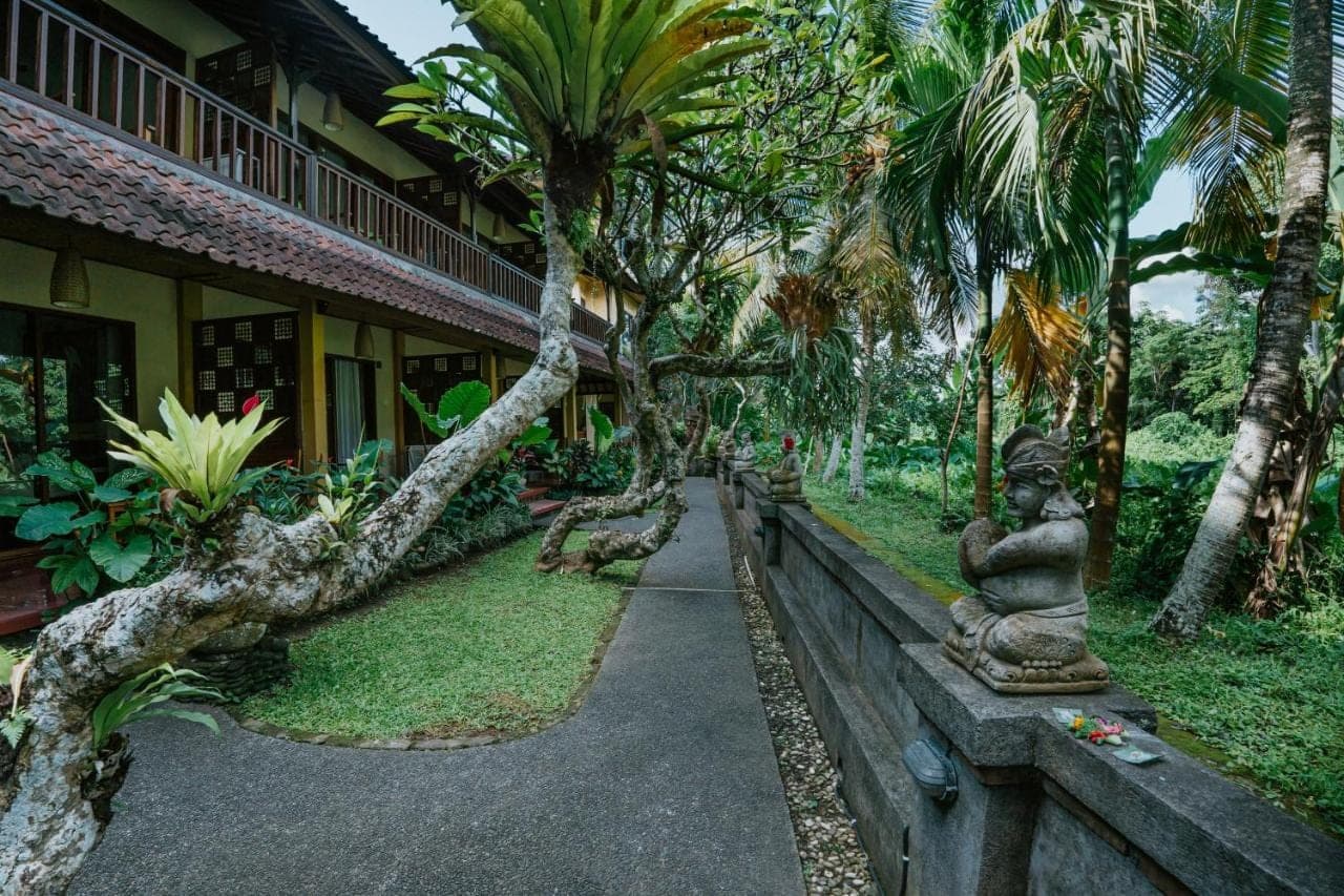 a statue in front of a building with palm trees at Jati Home Stay in Ubud
