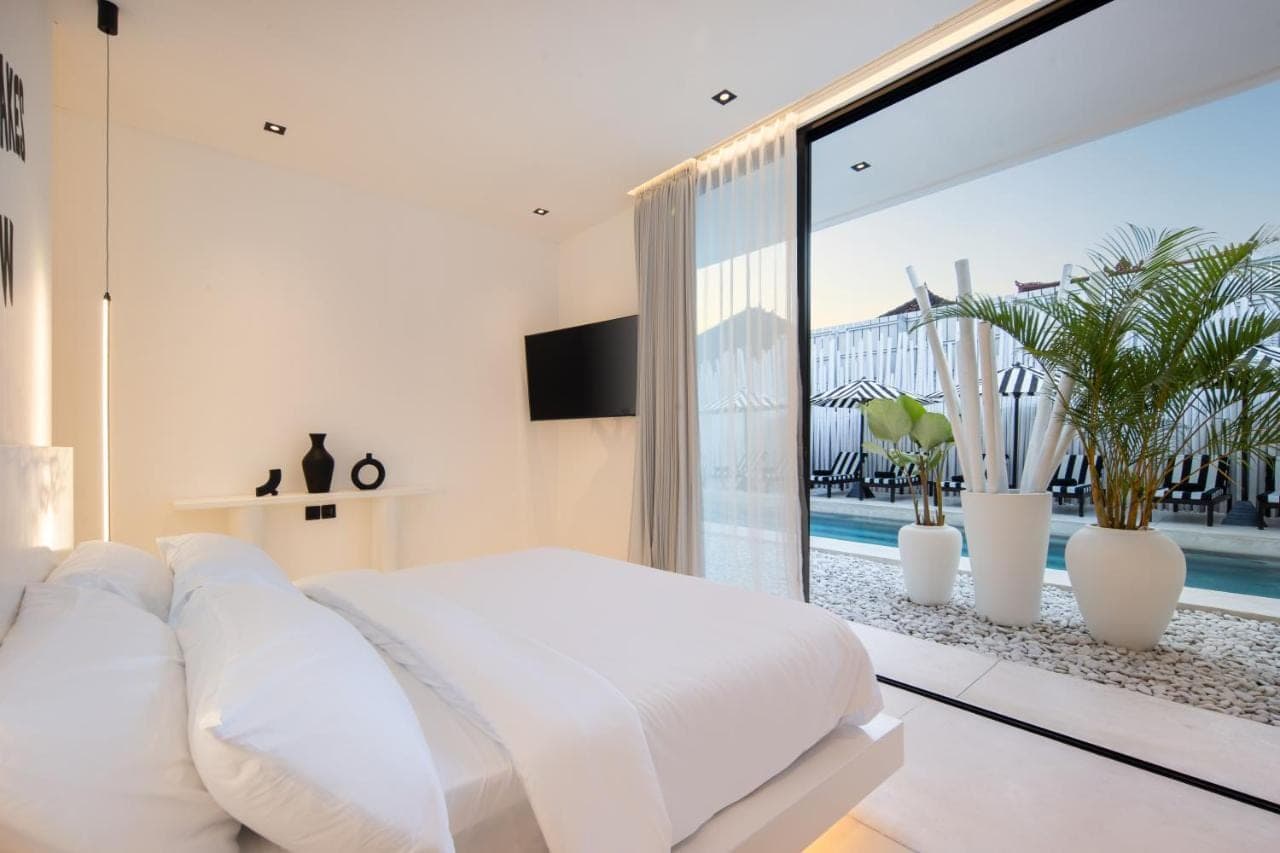 a bedroom with a white bed and a large window at The Den Canggu in Canggu