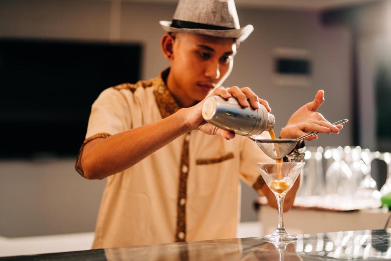 a man in a hat is making a cocktail at Mejore Beach Hotel in Amed