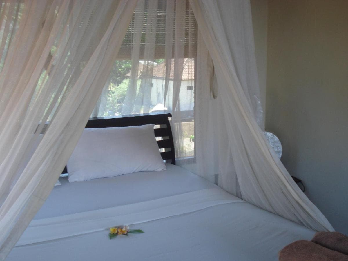 a bed with a canopy and a window with flowers on it at Bulih Beach Bungalows in Amed