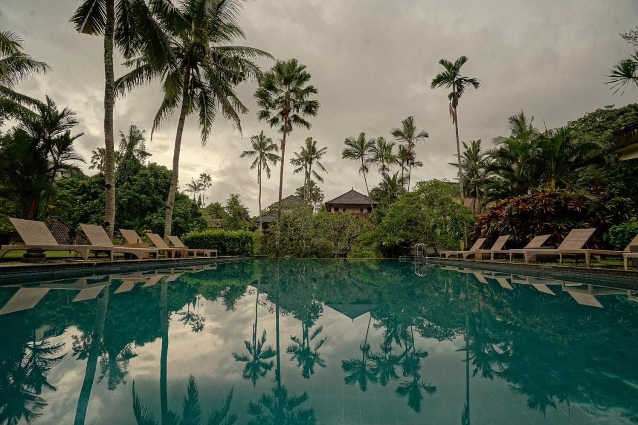 a swimming pool with chairs and palm trees at Pertiwi Resort &amp; Spa in Ubud