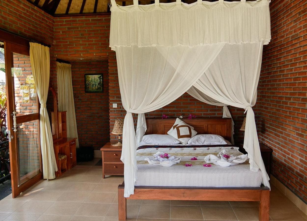 a bedroom with a canopy bed with white curtains at Embang Homestay in Sidemen
