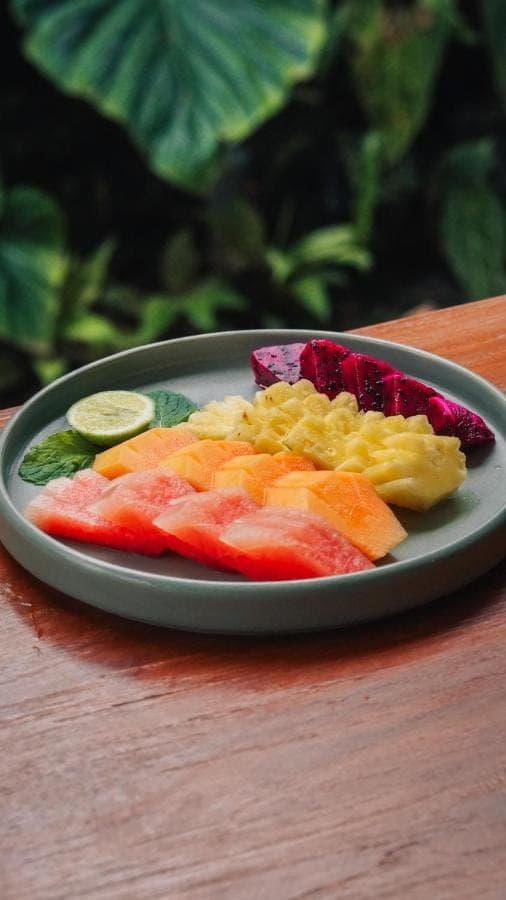 a plate of food with fruit on a table at Myraga House Ubud in Ubud