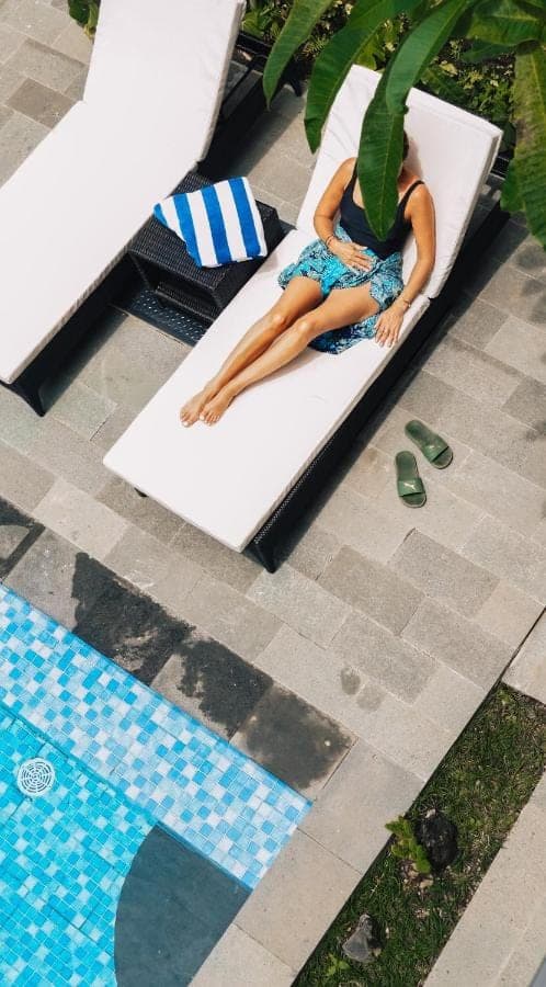 a woman laying on a bed next to a swimming pool at Myraga House Ubud in Ubud